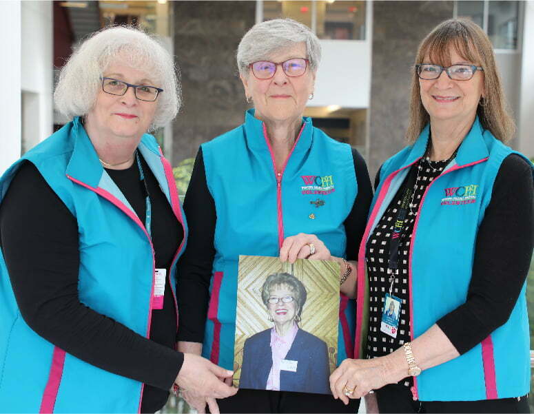 Three senior women, all wearing blue Women's College Hospital vests hold the picture of Maureen Green.